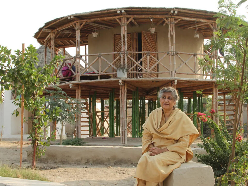 Yasmeen Lari stands beside the women's centre she designed in Sindh province, elevated on stilts to withstand floods. This remarkable structure is crafted from bamboo, mud, and lime, showcasing her innovative architectural approach.