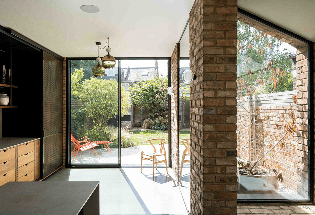 A modern, sunlit home extension with large glass windows and exposed brick columns, offering a seamless connection to the outdoor garden. This design showcases how client involvement through technology can enhance personalisation and transparency in architectural projects.