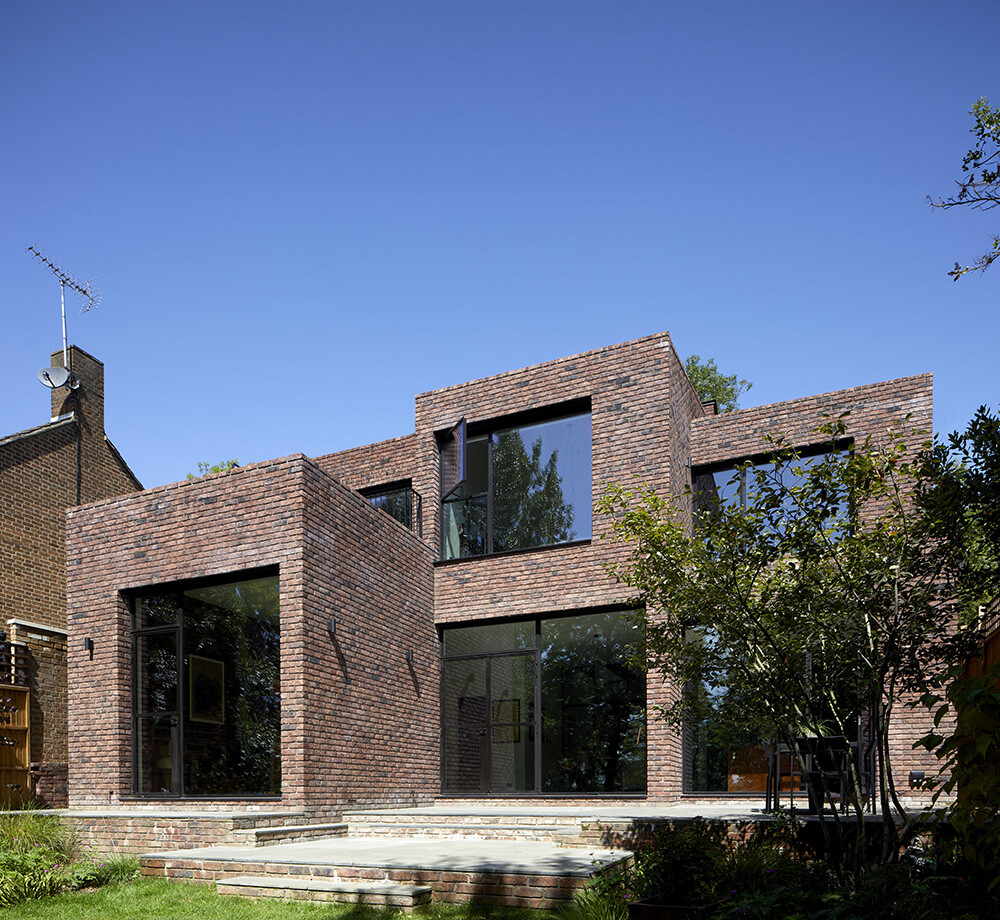 Modern brick extension with large glass windows, showcasing contemporary design while adhering to planning and building regulations, surrounded by greenery in a residential garden.