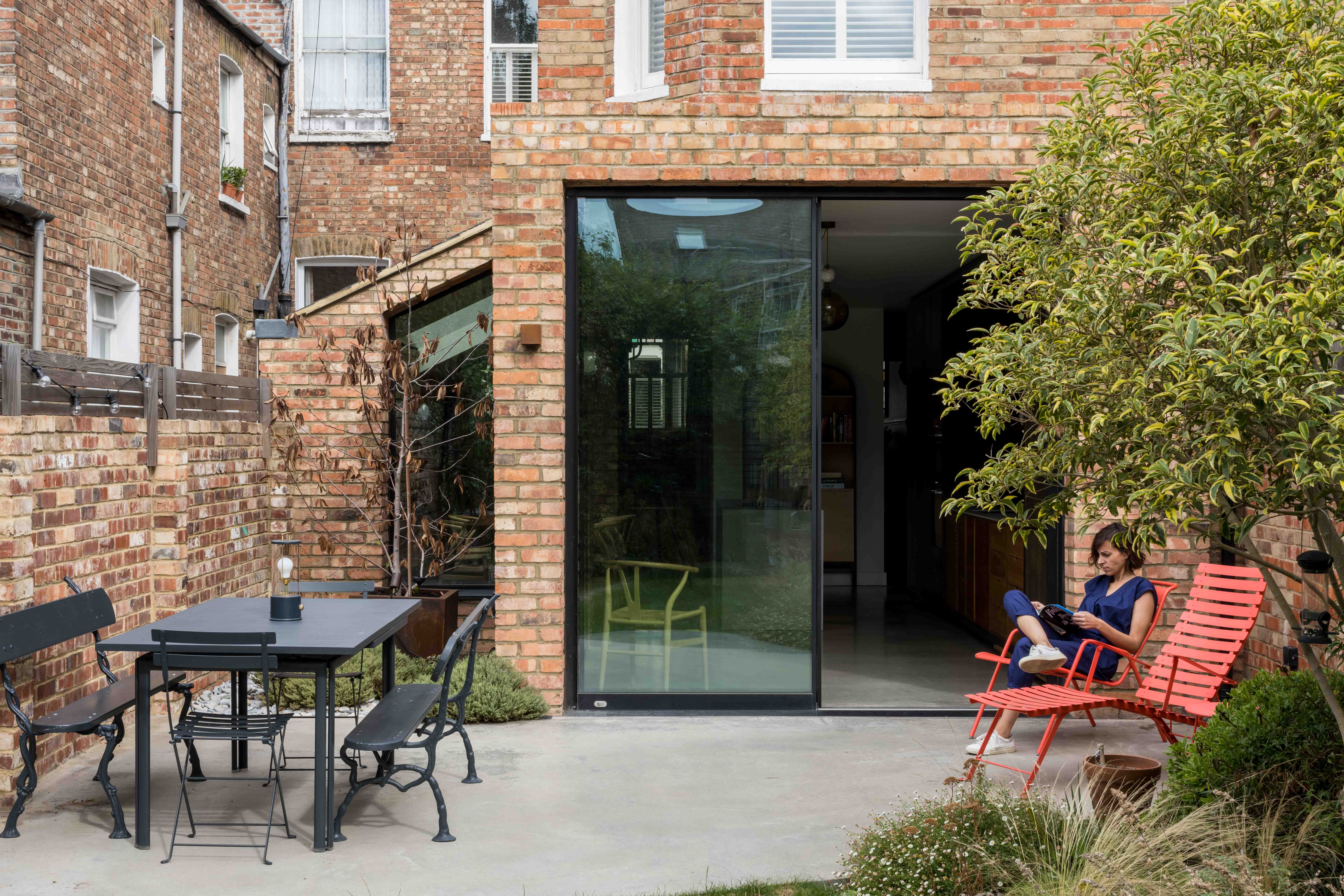 Modern London house extension with glass sliding doors, brick exterior, and a stylish garden seating area, highlighting themes of house extension costs and design in 2024.