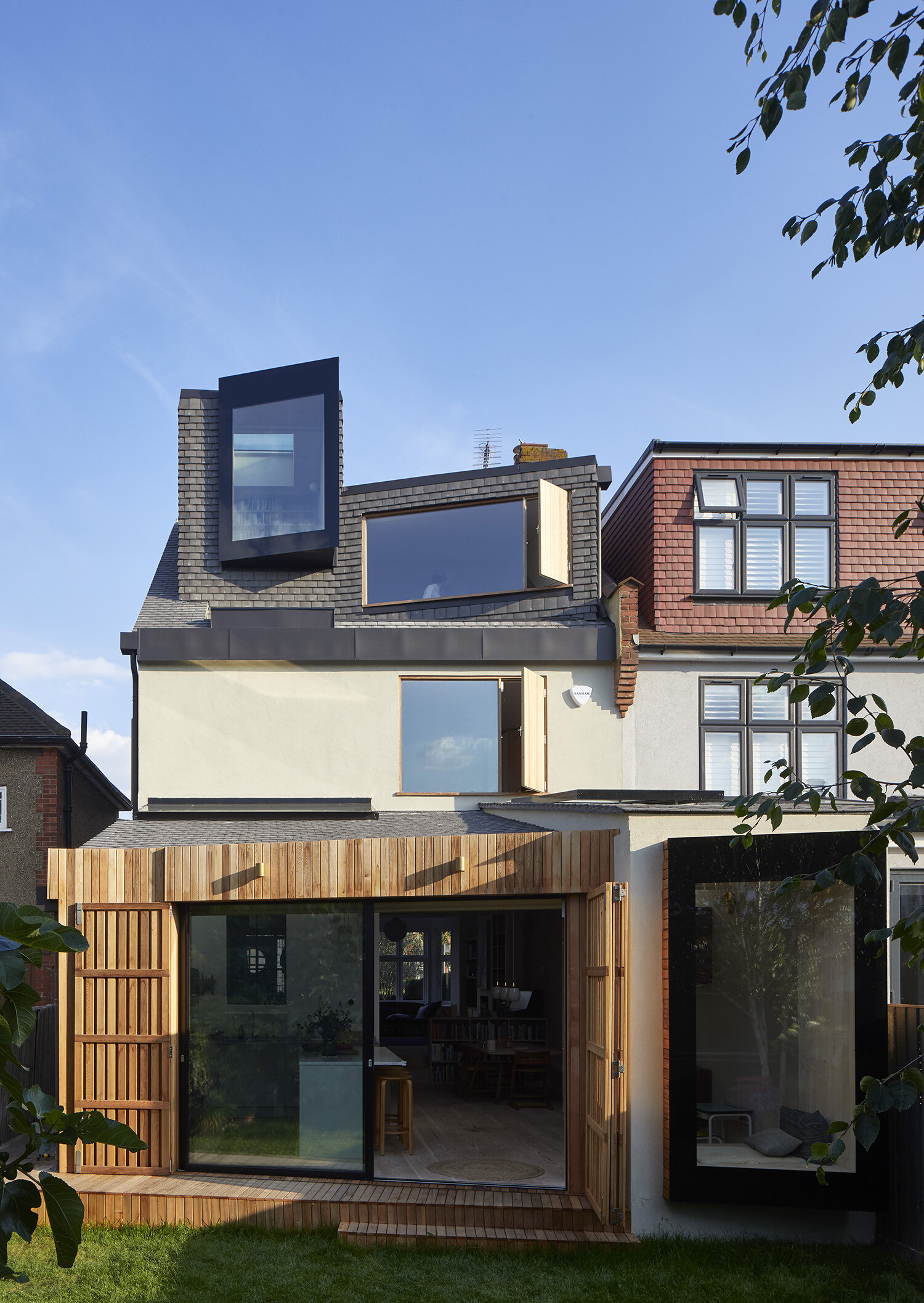 Modern semi-detached house extension featuring a striking loft conversion with angular windows, a timber-clad ground floor addition, and seamless integration of contemporary and traditional design elements.