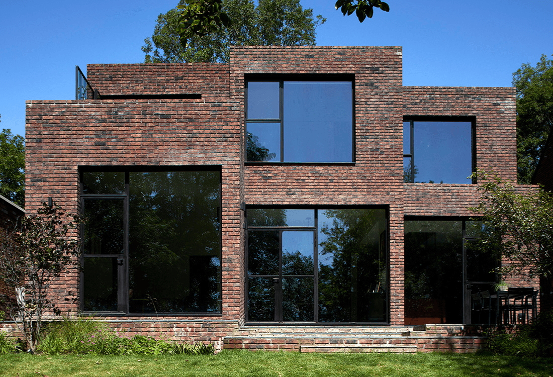 Contemporary brick home featuring geometric design and expansive glass windows, exemplifying innovative architecture that blends modern aesthetics with natural surroundings.