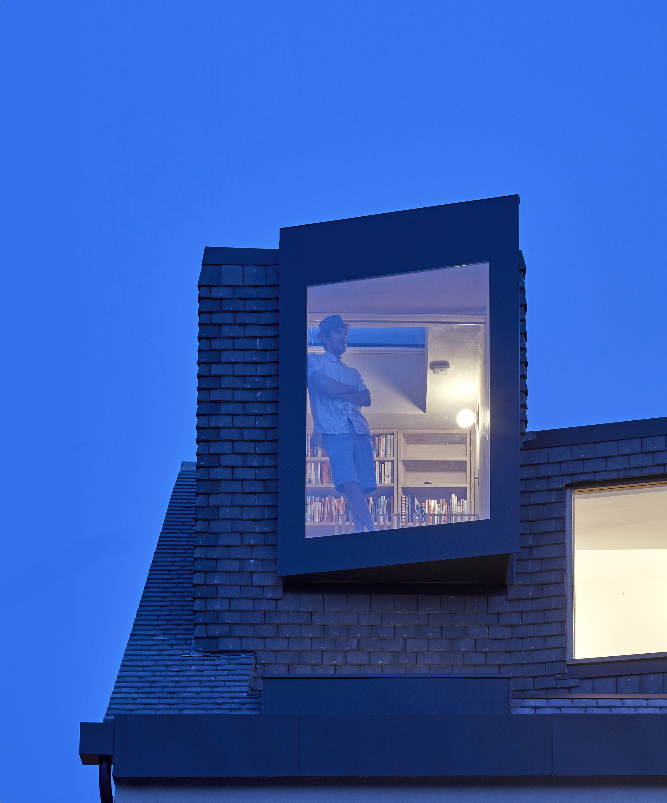 A man watching out of the window from his loft that has been converted into a library. 